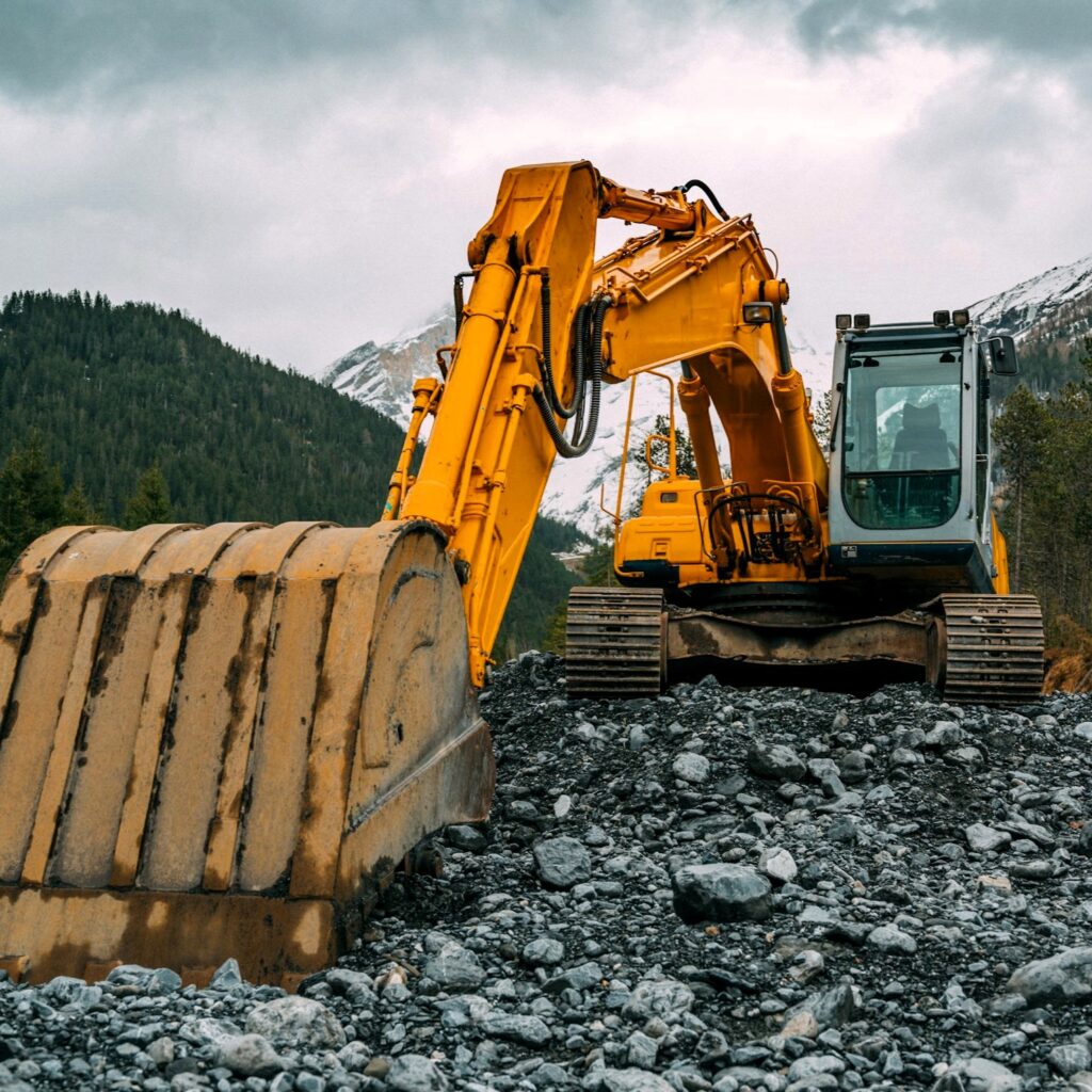 Großer gelber Kettenbagger mit Baggerlöffel auf einer Baustelle mit Schotter im Wald Stockfoto
